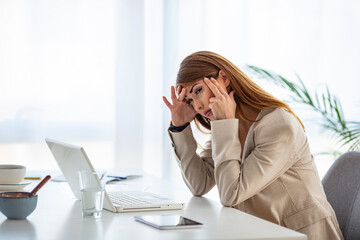 Depressed businesswoman rubbing eyes in office. Portrait of depressed young businesswoman sitting at computer in office rubbing eyes. Overworking concept