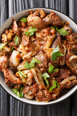 Armenian cuisine fried chicken offal tzhvzhik with onions, tomatoes and spices close-up in a bowl. vertical top view