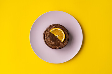 Delicious chocolate pancakes with slices of orange for breakfast on a pink plate on yellow background. Fresh, sweet and healthy dessert. 