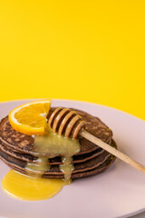 Chocolate pancakes with liquid honey slice of orange for breakfast on yellow background. Vertical. 