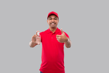 Fototapeta na wymiar Indian Delivery Man Holding Hands Sanitizer Showing Thumb Up. Hands Antiseptic. Man in Red T shirt. Health, Isolation Concept