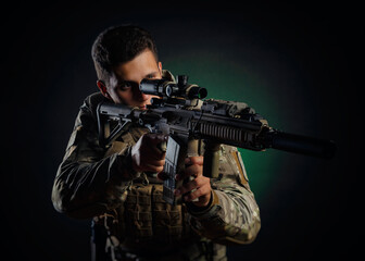 Fototapeta premium a brutal guy in military airsoft overalls poses with a weapon in his hands on a dark background