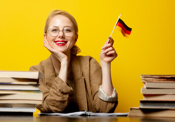 Style blonde woman sitting at table with books and flag of Germany on yellow background