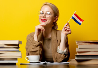 Style blonde womansitting at table with books and flag of Netherlands on yellow background