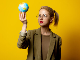 Style blonde woman in jacket hold Globe on yellow background