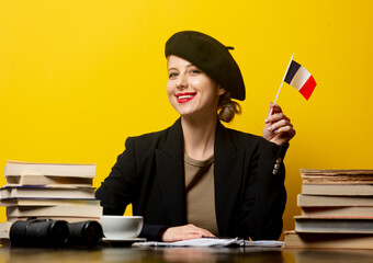 Style blonde woman in beret with French flag and books around on yellow background