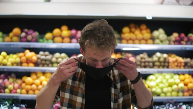 A young man puts on a tissue mask to protect against the epidemic, a close-up portrait. Protection from the coronavirus pandemic. Standing against grocery shelves