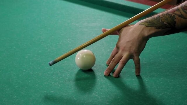 Close-up of a man playing pool in a dark bar, he hits the ball with a cue and hits the hole. Playing Billiards on the green table.
