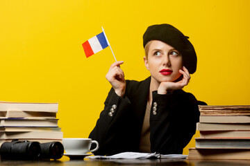 Style blonde woman in beret with French flag and books around on yellow background