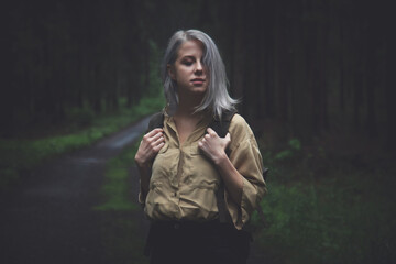 Blonde woman with backpack in rainy day in forest