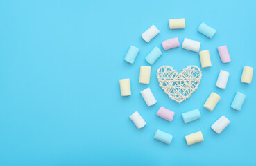 White rattan heart and delicious marshmallows on blue background. Happy day, breakfast, love, good morning concepts. Valentine greeting card. Flat lay style.