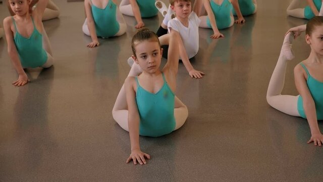 The training of young dancers in the ballet studio. Young dancers perform gymnastic exercises during a warm-up in the classroom. Sport, gymnastics, child development.