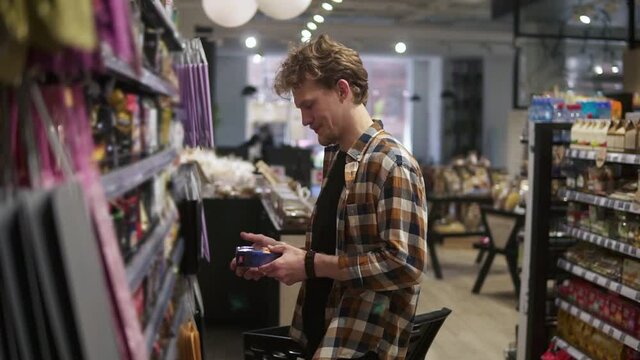 Customer in the supermarket. Man choosing, picking the pack of the coffee. Shelves on the background. Side view