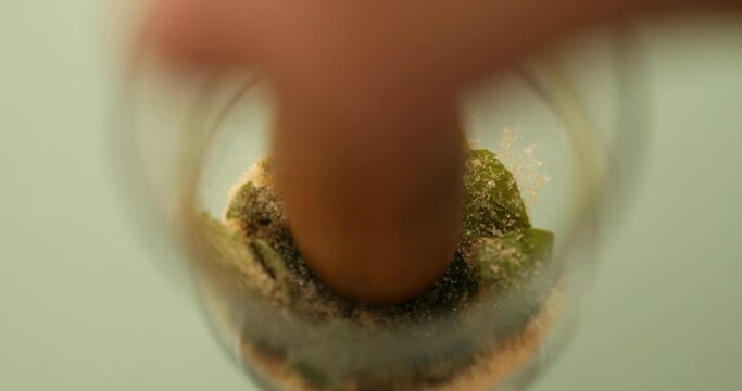 Mashing mint and sugar in glass with muddler to make mint mojito coffee
