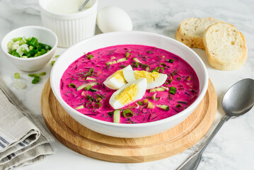 Homemade cold beetroot soup with boiled egg  in a white plate on a marble table. Selective focus