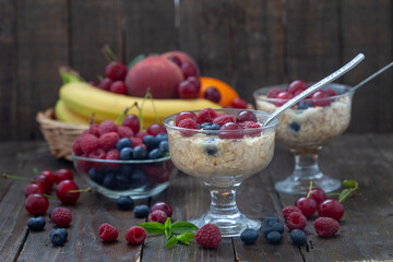 Oatmeal porridge in bowl topped with fresh blueberries, raspberries and cherries. Lot of fruits in background. Healthy eating concept.