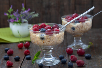 Oatmeal porridge with fresh blueberries, raspberries and cherries in glass bowl on wooden table. Healthy breakfast, healthy eating, vegan food concept.