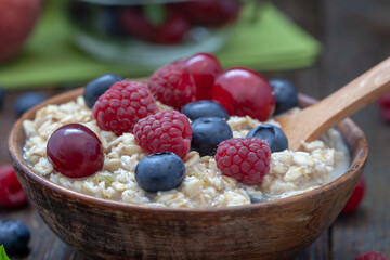 Rolled oats with blueberries and raspberries, closeup Healthy breakfast cereal oat flakes in bowl on wooden table.