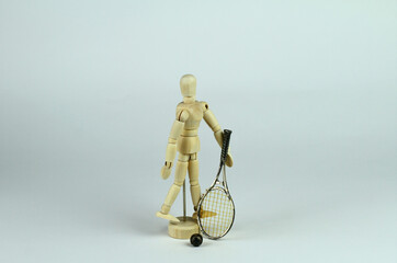 Wooden mannequin walking with a tennis racket in his hand, light background.