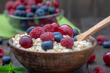 Rolled oats with blueberries and raspberries. Healthy breakfast cereal oat flakes in wooden bowl with wooden spoon.