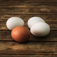 Three white eggs and one dark egg on wooden table.