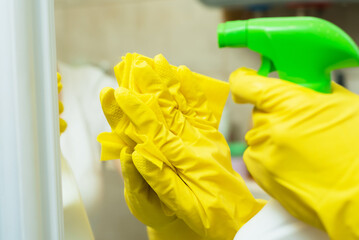 A girl is washing a mirror in yellow gloves. A girl is cleaning a mirror with detergents