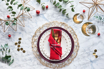 Christmas table setting with gold utensils in folded textile napkin and fresh eucalyptus on marble background. Flat lay on table with golden cutlery, white plates and geometric hexagons.
