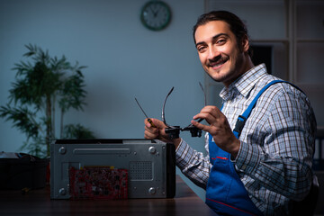 Young male technician repairing computer in workshop at night
