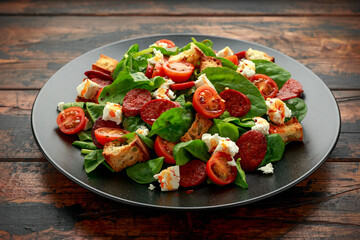 Chorizo Tomato salad with spinach, feta cheese and croutons on black plate. healthy summer food