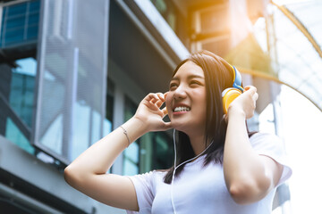 Young woman using headphone for listening nice music in city with building background with toothy...