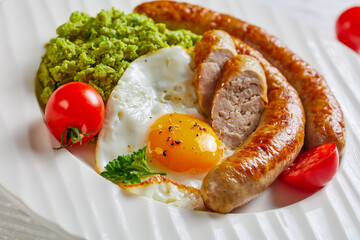 Pork sausages, egg, green pea on a white plate