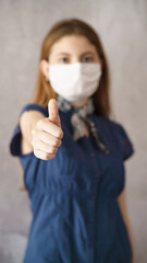 Young woman showing thumb up with face protective mask