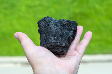 Male hand with a piece of coal on a blurred background of green forest