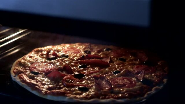 View from inside of the oven. Cooking italian pizza in electric convection oven. Closeup of pizza topped with tomatoes, olives and ham mozzarella and cheese. Pizza cheese melting and bubbling. Timelap
