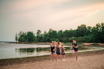 Children and adult girls run along the coast in sportswear on a background of nature at sunset