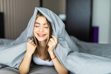 Smiling young woman under a duvet in her bedroom