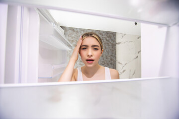 Fototapeta na wymiar Young shocked woman looking in empty fridge at home