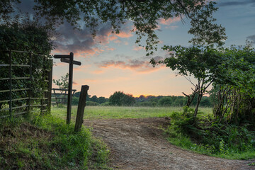Stunning English countryside Summer sunset landscape image with footpath signposted through warm field