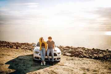 Romantic couple is standing near a Muscle car on the beach. The handsome bearded man and an...