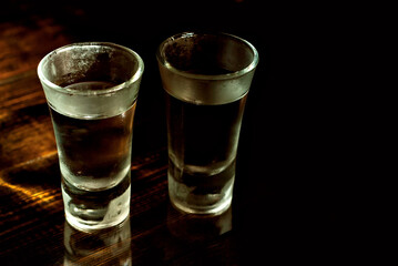 Two frozen glasses close up. Glasses with alcohol on a black wooden table. Vodka on a dark contrasting background.