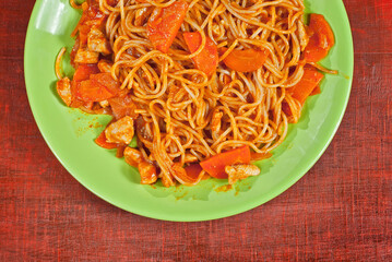 Pasta with carrots in a green plate on a wooden table. Vermicelli with orange sauce on red plywood.