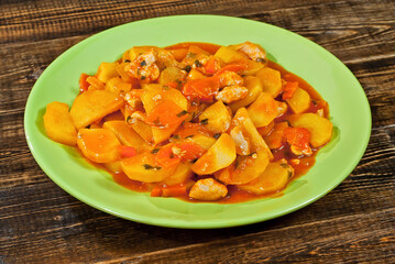 Potatoes in a green plate on a wooden table. Boiled potatoes with orange sauce on a brown board.