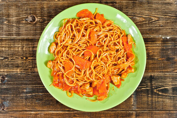 Pasta with carrots in a green plate on a wooden table. Vermicelli with orange sauce on a black shabby board.