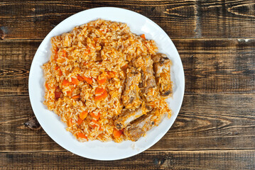 Pilaf with meat and carrots in a green plate. Rice on a brown shabby board. Place for text and copy space near food.