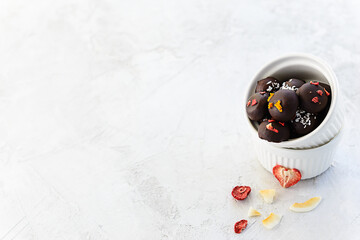 Chocolate sweets made from oatmeal, walnuts and raisins, coated with freeze-dried berries and coconut in a white bowl. Horizontal orientation, copy space. Sugar free, gluten, lactose.
