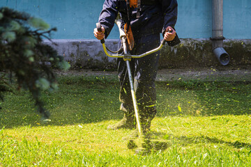 A man mows the grass with a gasoline scythe