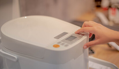 Female hand pushing on the button of the new modern rice cooker in the kitchen for preparing the...