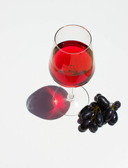 glass of red wine and red grape on white background with sparkling shadows. Free copy space.  Concept of organic drinks. Top view.