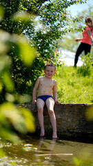 Portrait of a funny little boy sitting near water outdoors
