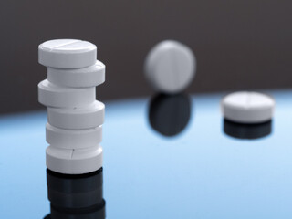 A stack of round tablets and two pills separately on a mirror surface. Medical background with medicines for business, industry, drugstores, clinics, hospitals.